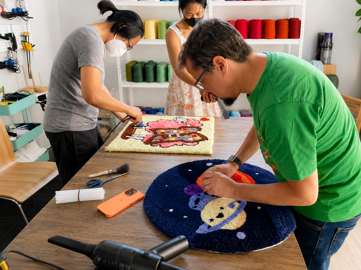 A tufted rug being trimmed and finished by hand on a studio worktable